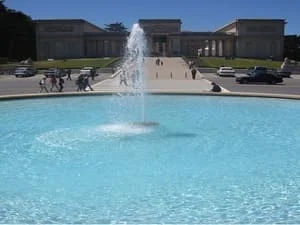 Large circular turquoise pool with a central fountain jet and light stone surrounding deck