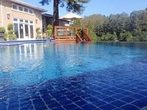 In-ground pool with dark blue mosaic tile and wooden deck steps with railings