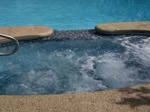 In-pool spa with bubbling jets, blue tile interior, tan stone coping, and stainless steel handrail
