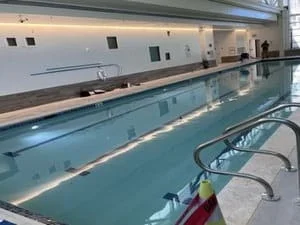Indoor lap pool with dark tile coping, stainless steel ladder, and recessed overhead lighting