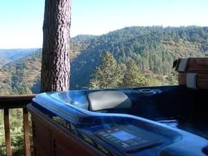 Wood-paneled hot tub with digital control panel on a wooden deck overlooking forested hills